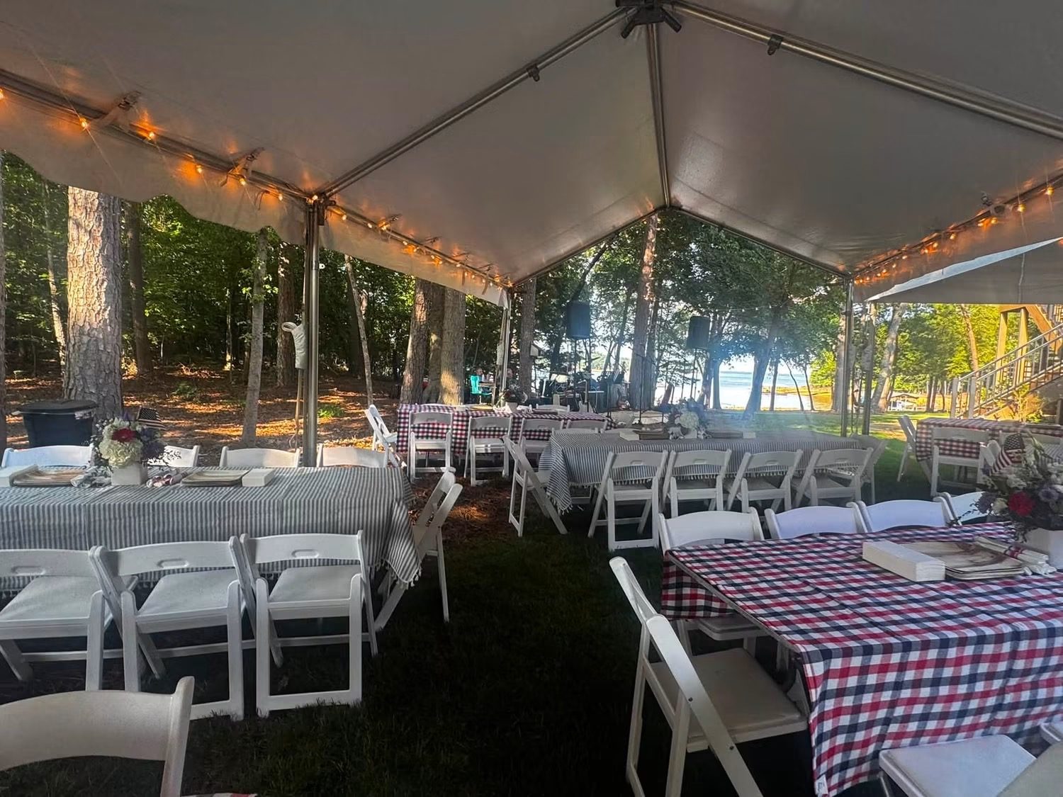 Long tables under a marquee strung with lights, white folding chairs and gingham cloths, the lake glowing through the pines at golden hour